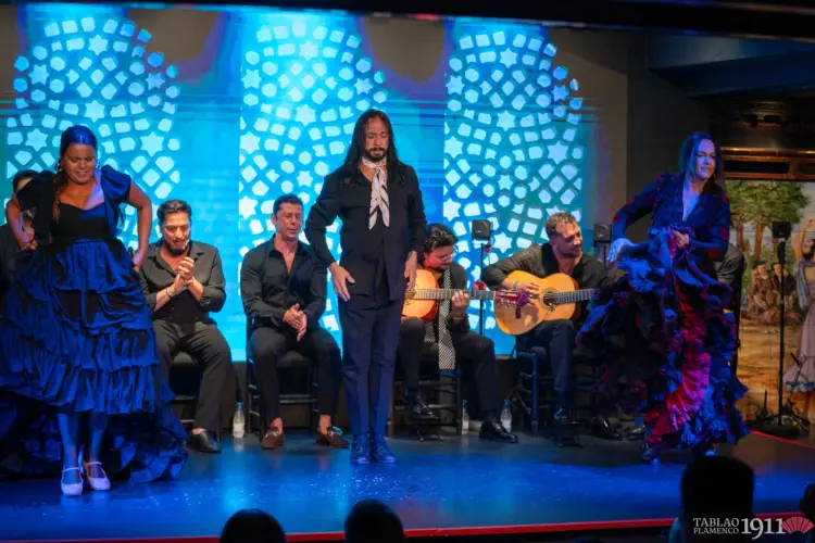 Fotografía de un auténtico cuadro flamenco en directo en un tablao de Madrid. Un cantaor, un guitarrista y una bailaora interactuando en el escenario en plena actuación, mostrando la conexión inseparable entre los tres pilares del arte jondo.