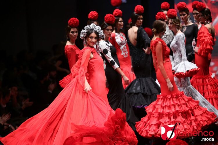 Modelos con trajes de flamenca y grandes flores rojas en el pelo durante un desfile de moda flamenca.